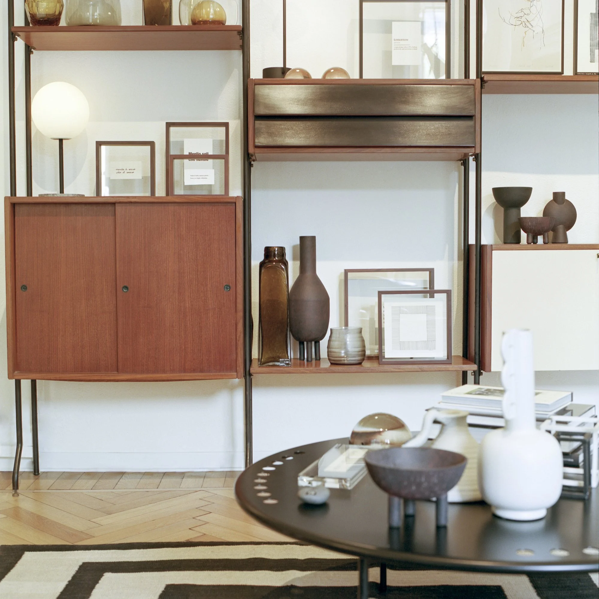 Display of decorative vases and framed artwork on shelves in a modern interior with a black round table in the foreground.