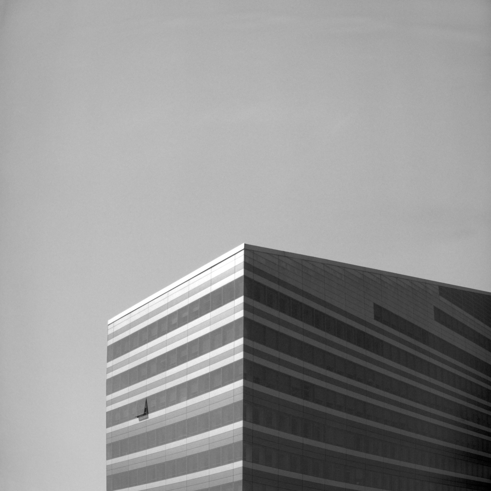 A modern multi-story building with dark glass windows and white trim, viewed from a low angle against a cloudy sky.