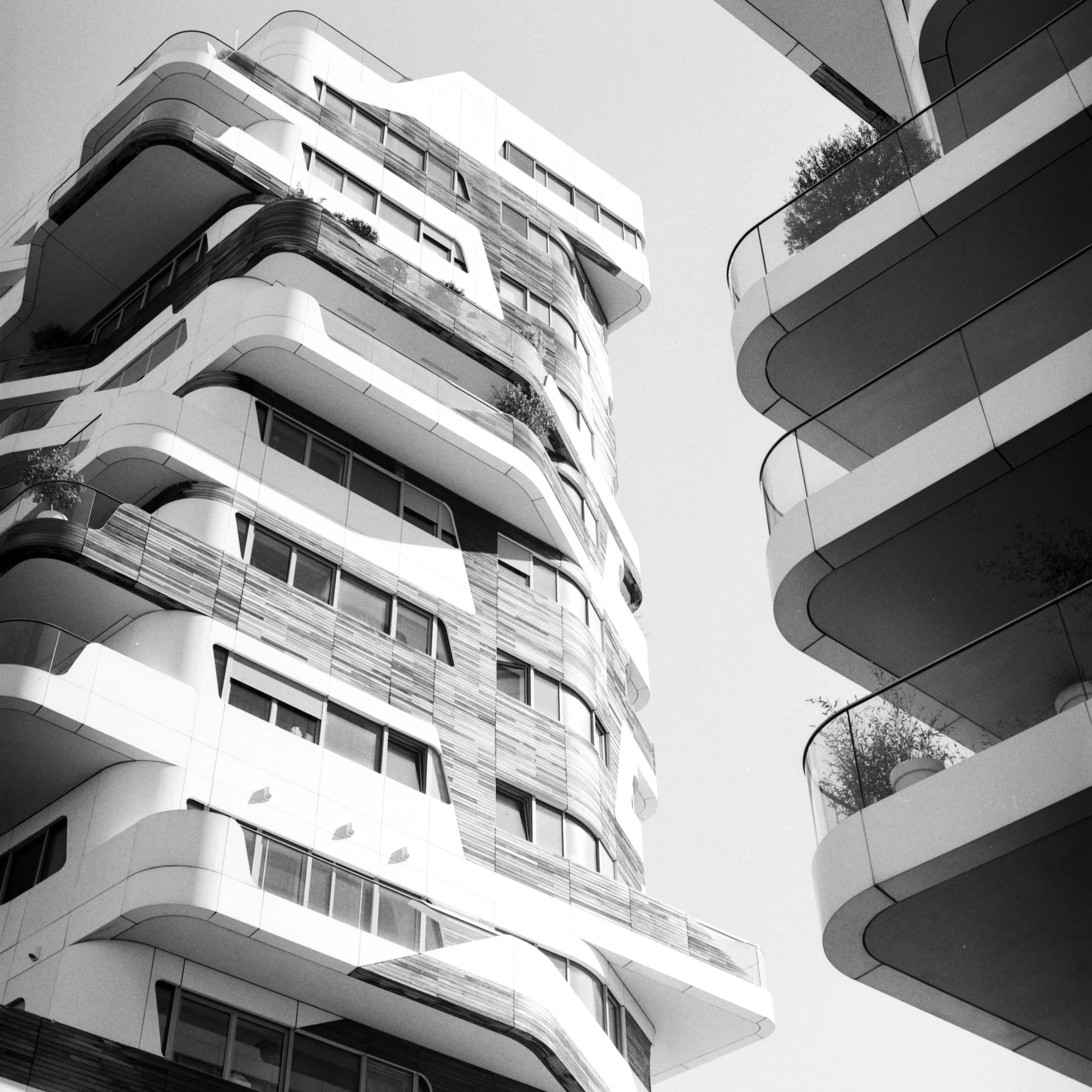 Black and white photograph of modern, multi-story residential building with rounded balconies and large windows.