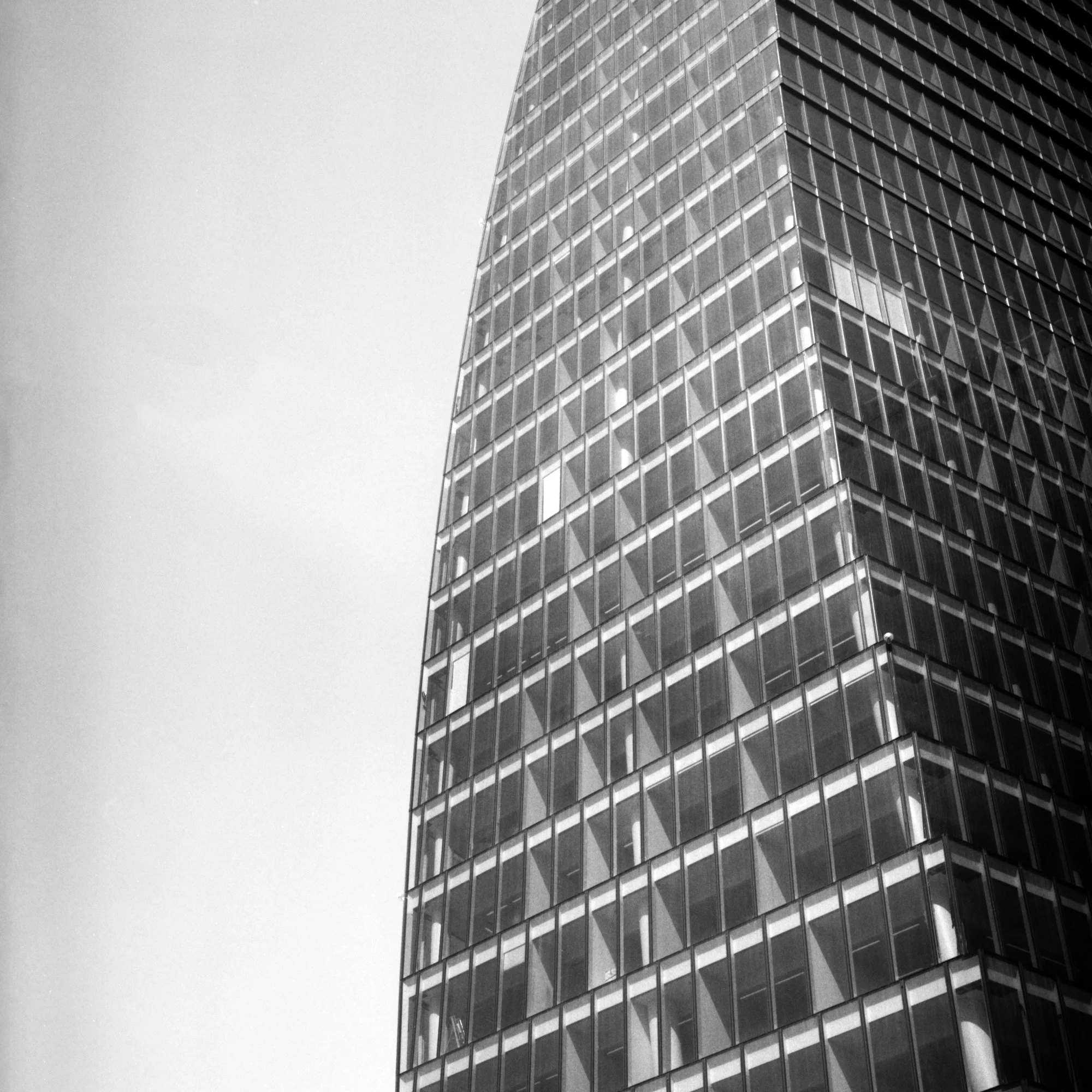 A tall modern glass building with a grid pattern of windows on its exterior, set against a cloudy sky.