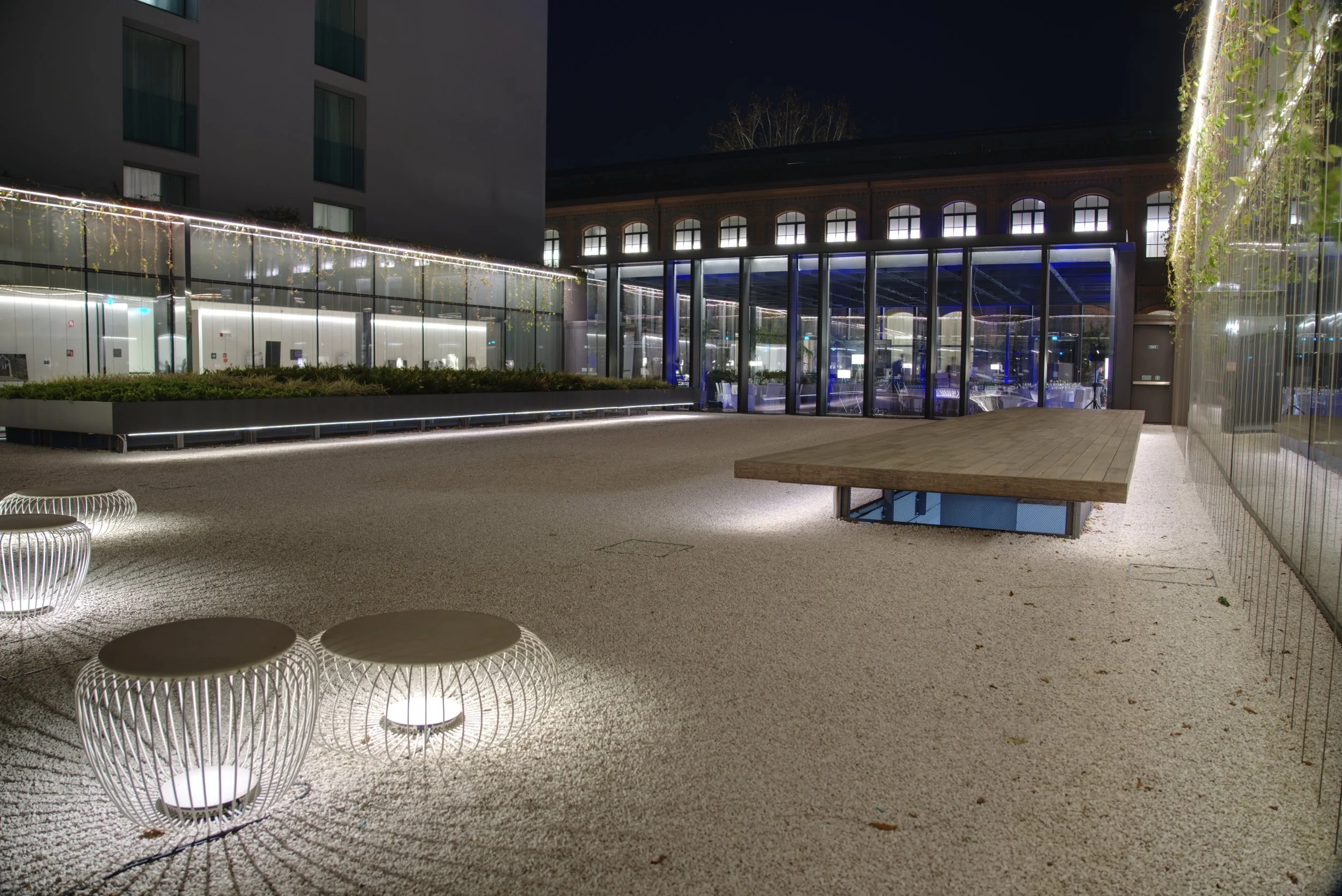 Outdoor terrace at night with modern seating, a glass enclosed area, and illuminated surroundings.