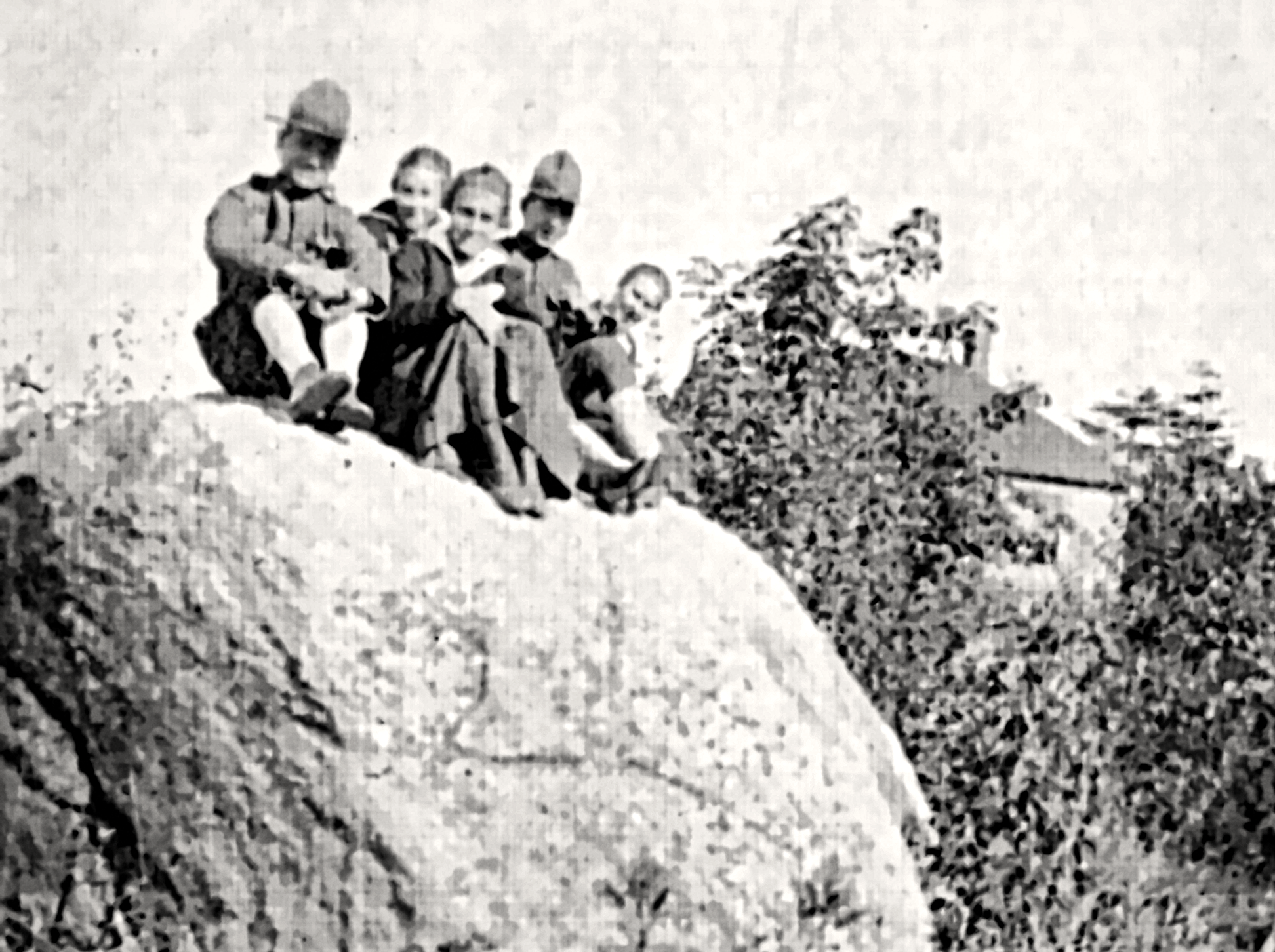 Black and white photo of five children sitting on a hillside, with trees in the background.