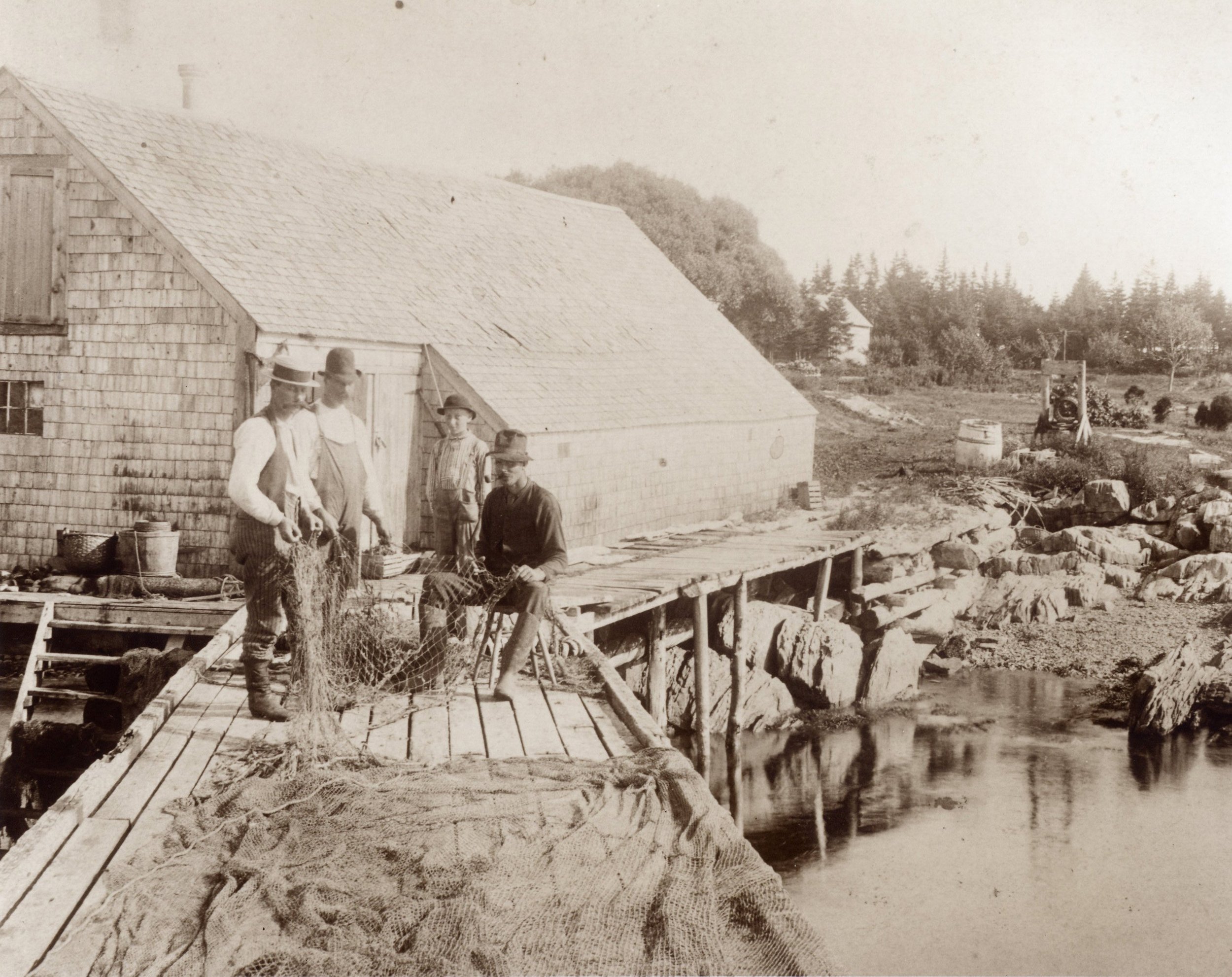Joe Rich, Ira Rich, Frank or Ed Woodbury, and Levi Alexander with fish nets on the wharf off a large barn at Harbor de Grace, 1892. Zoeth Henry Rich owned the large barns and ran a barter-system provision store in the Rich family home across the stre