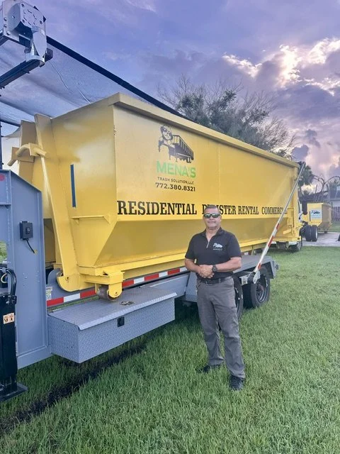 A man standing in front of a large yellow trash container attached to a truck, with the logo of 'MEMA'S Trash Solutions' and contact info, on a grassy area during sunset.