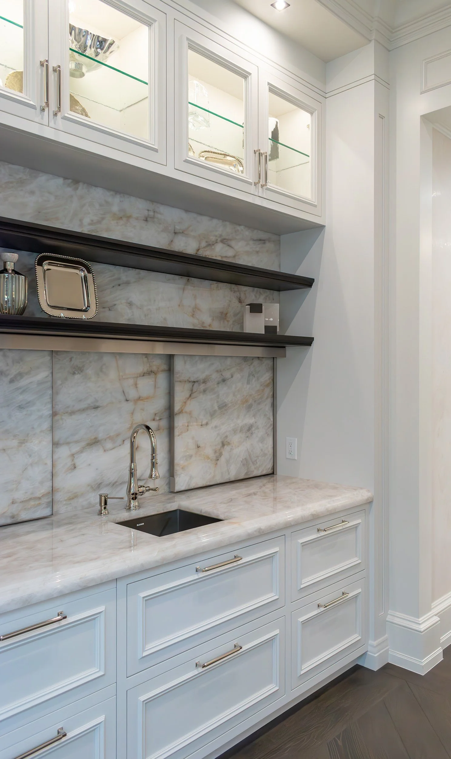 Painted cabinetry with glass-front uppers and a quartzite backsplash