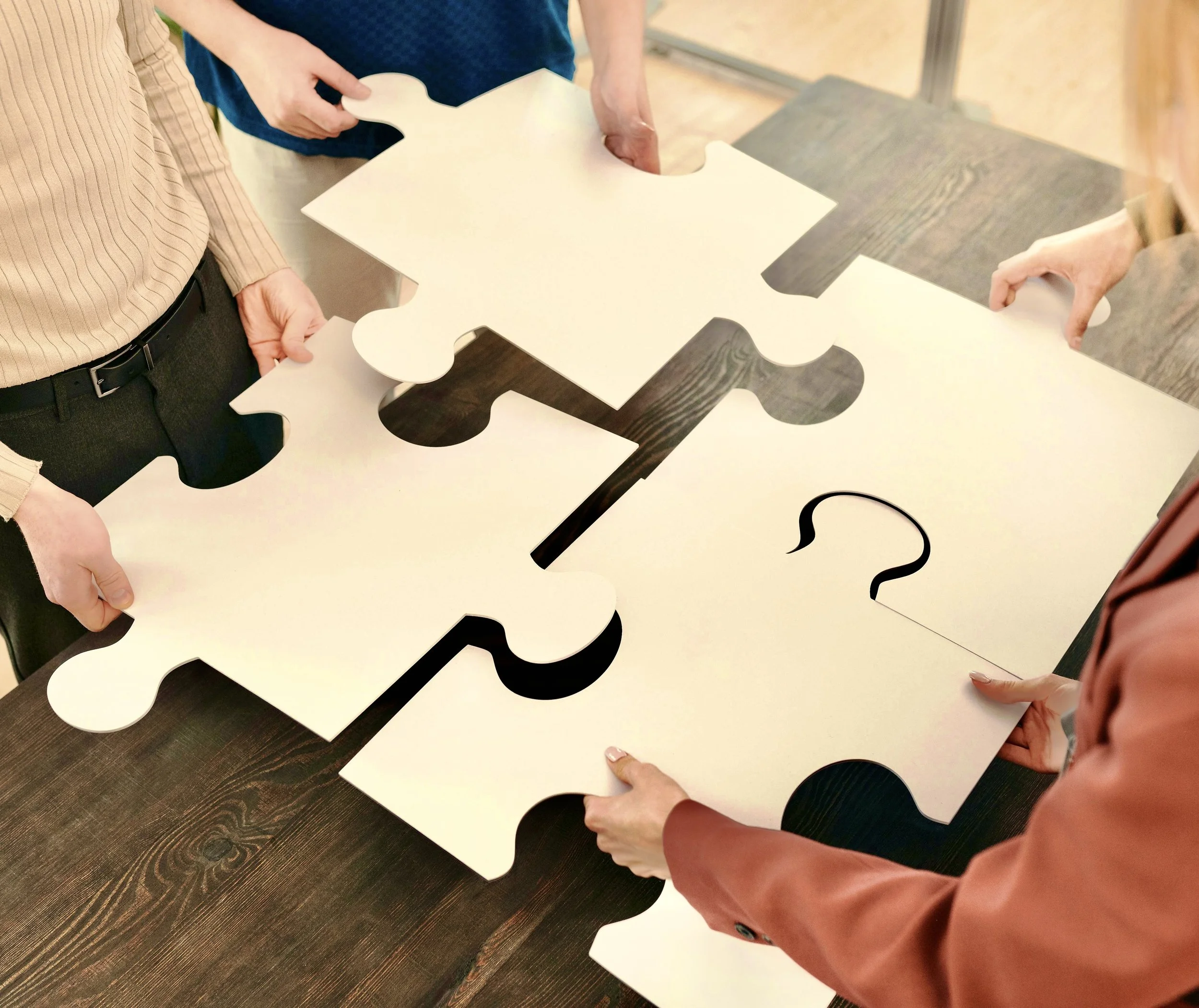 Persone che uniscono i pezzi di un puzzle bianco su un tavolo di legno.
