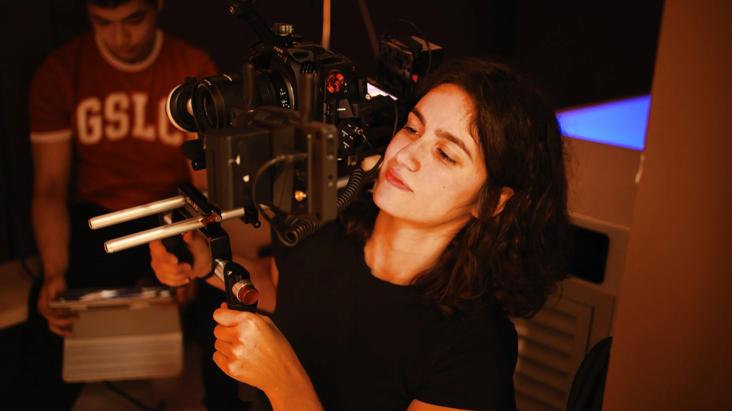 A woman operating a professional camera mounted on a stabilizer rig in a dimly lit room.