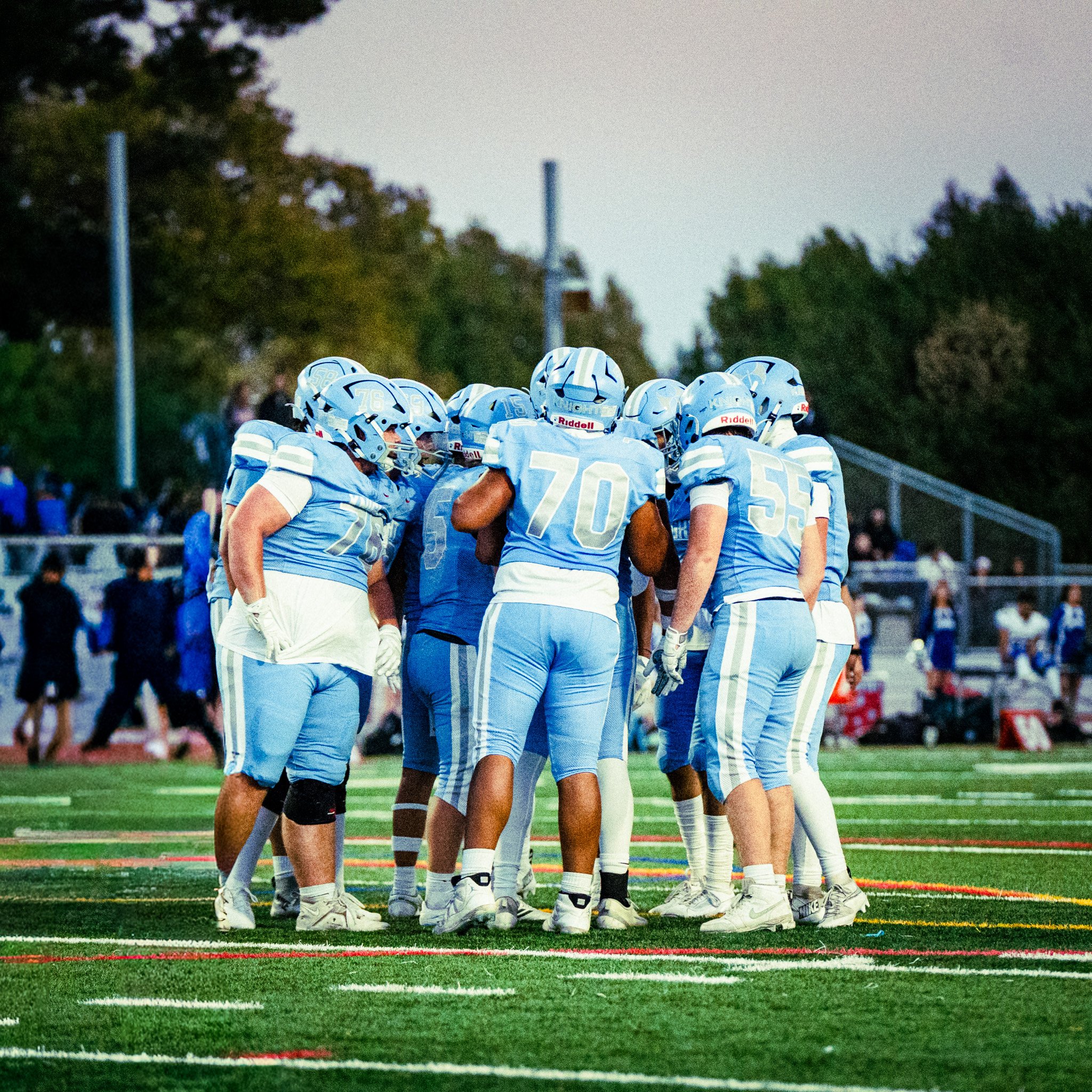 A group of football players in blue and white uniforms huddled together on a football field
