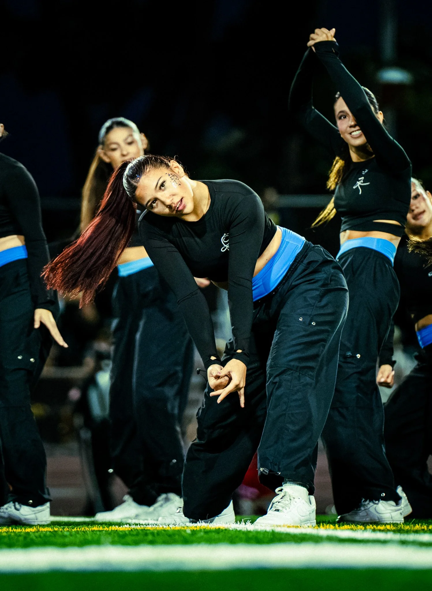Cheerleaders performing a dance routine on a football field during a nighttime game.