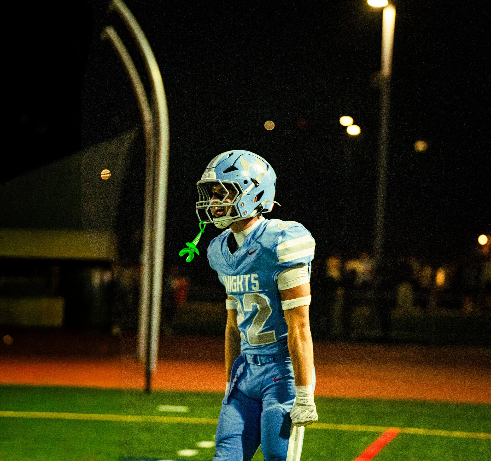 Football player wearing a blue helmet and a blue jersey with white and red accents on the field at night, near the goalpost.