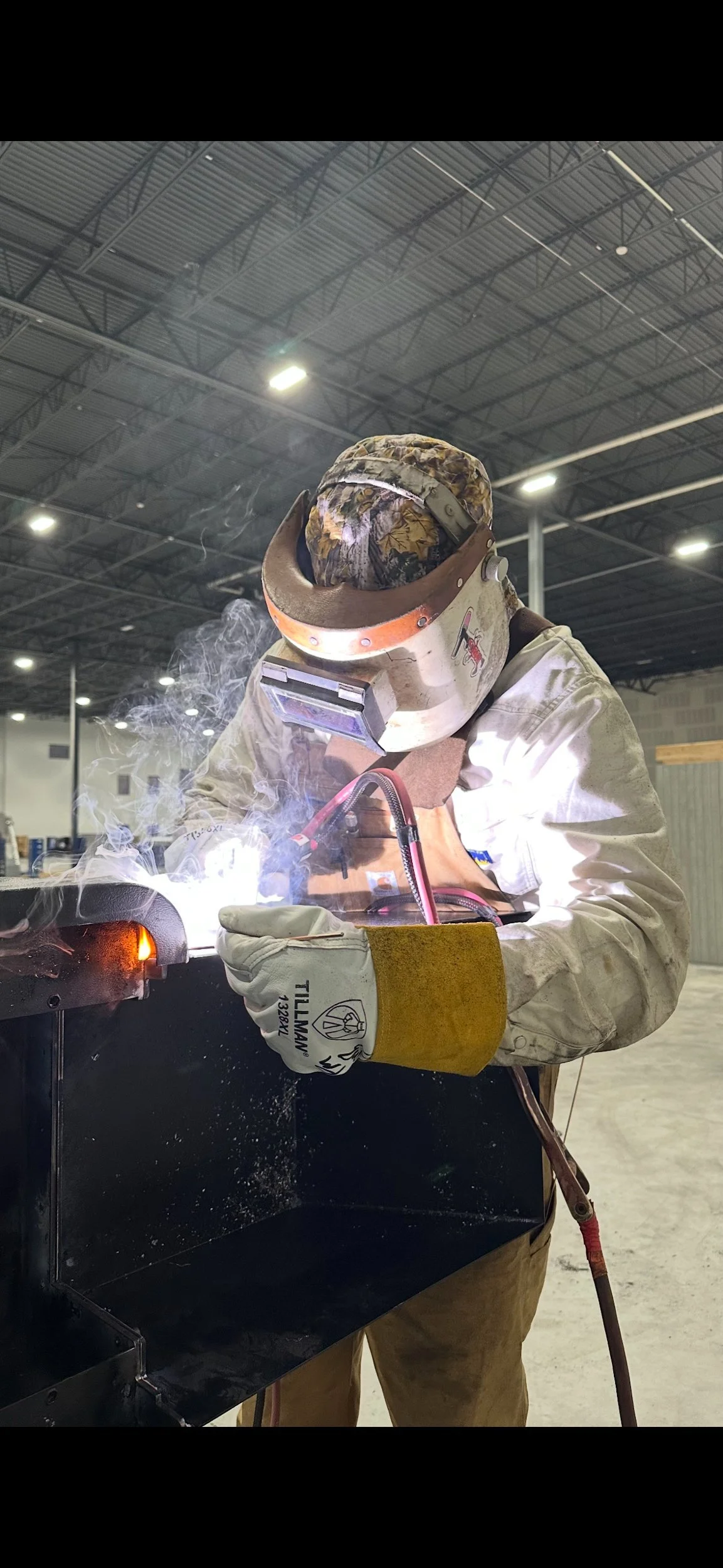 Certified TIG welder in full protective gear welding steel inside an industrial building