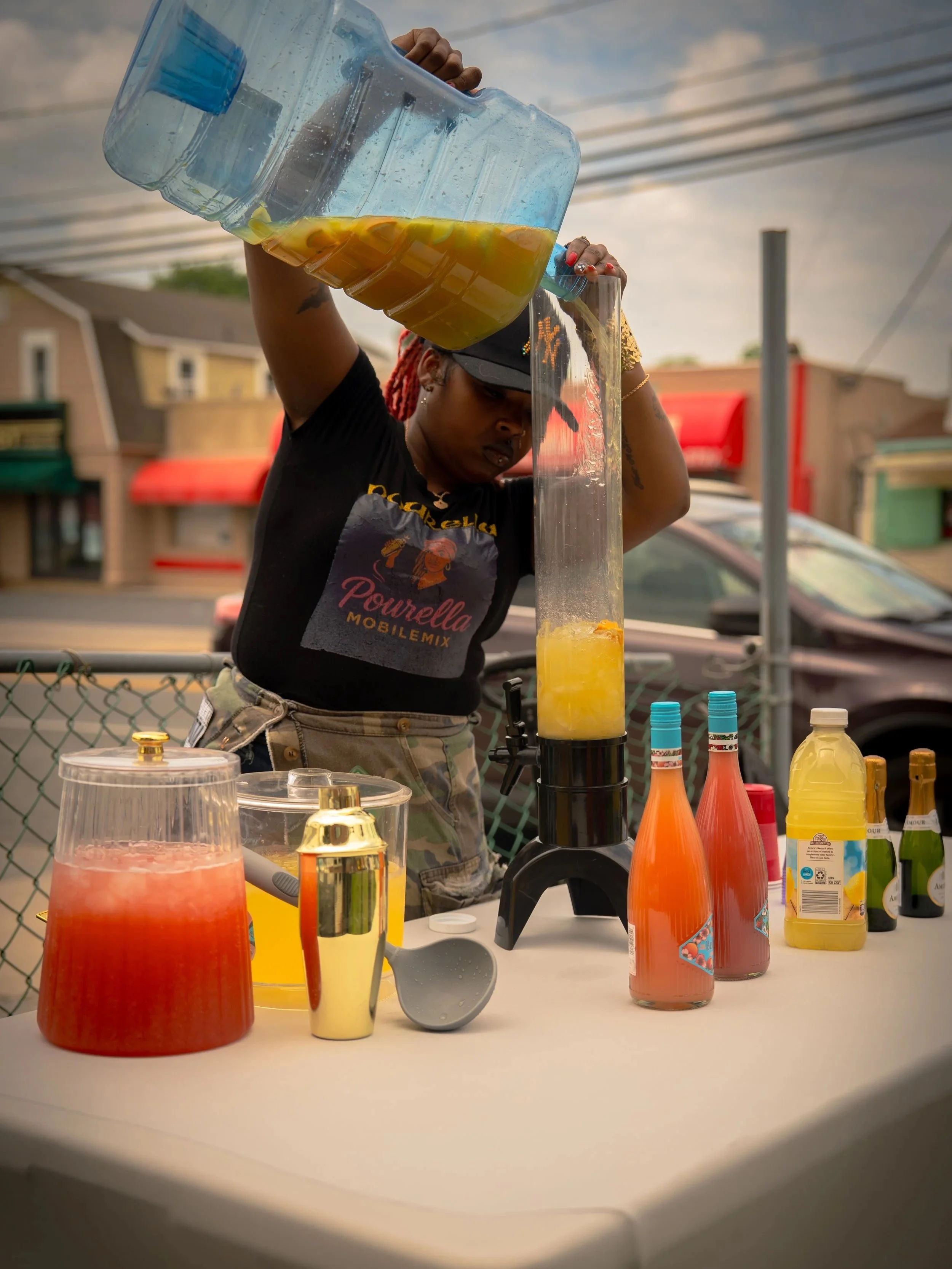 A woman making fresh fruit smoothies outdoors with various bottles of flavored syrup and other ingredients on the table.