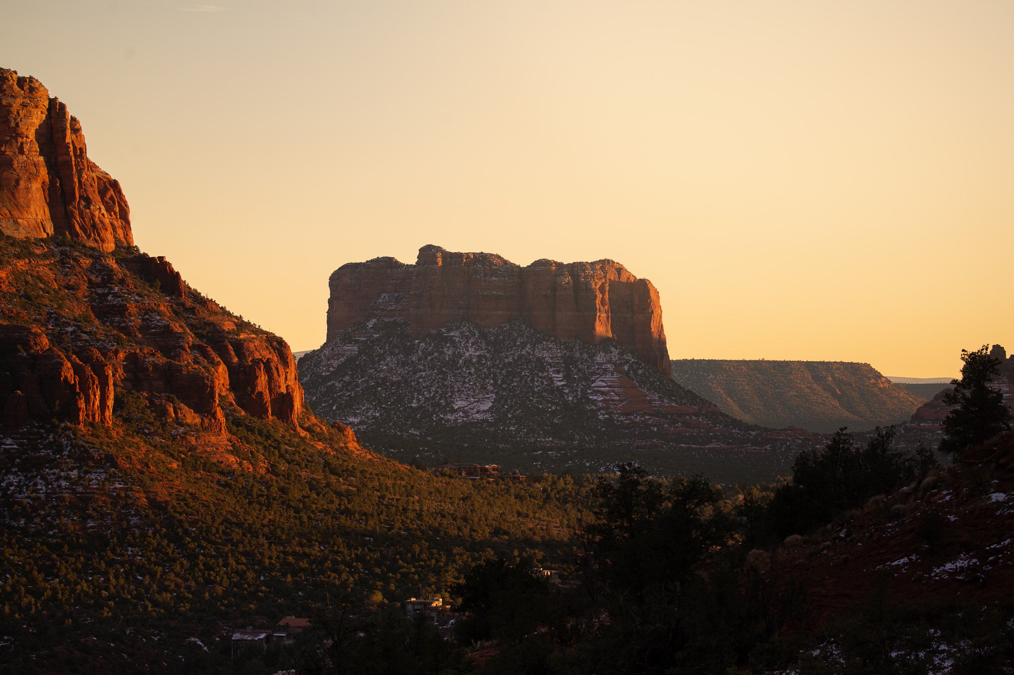 Sunset over a landscape of red rock formations and sparse trees.