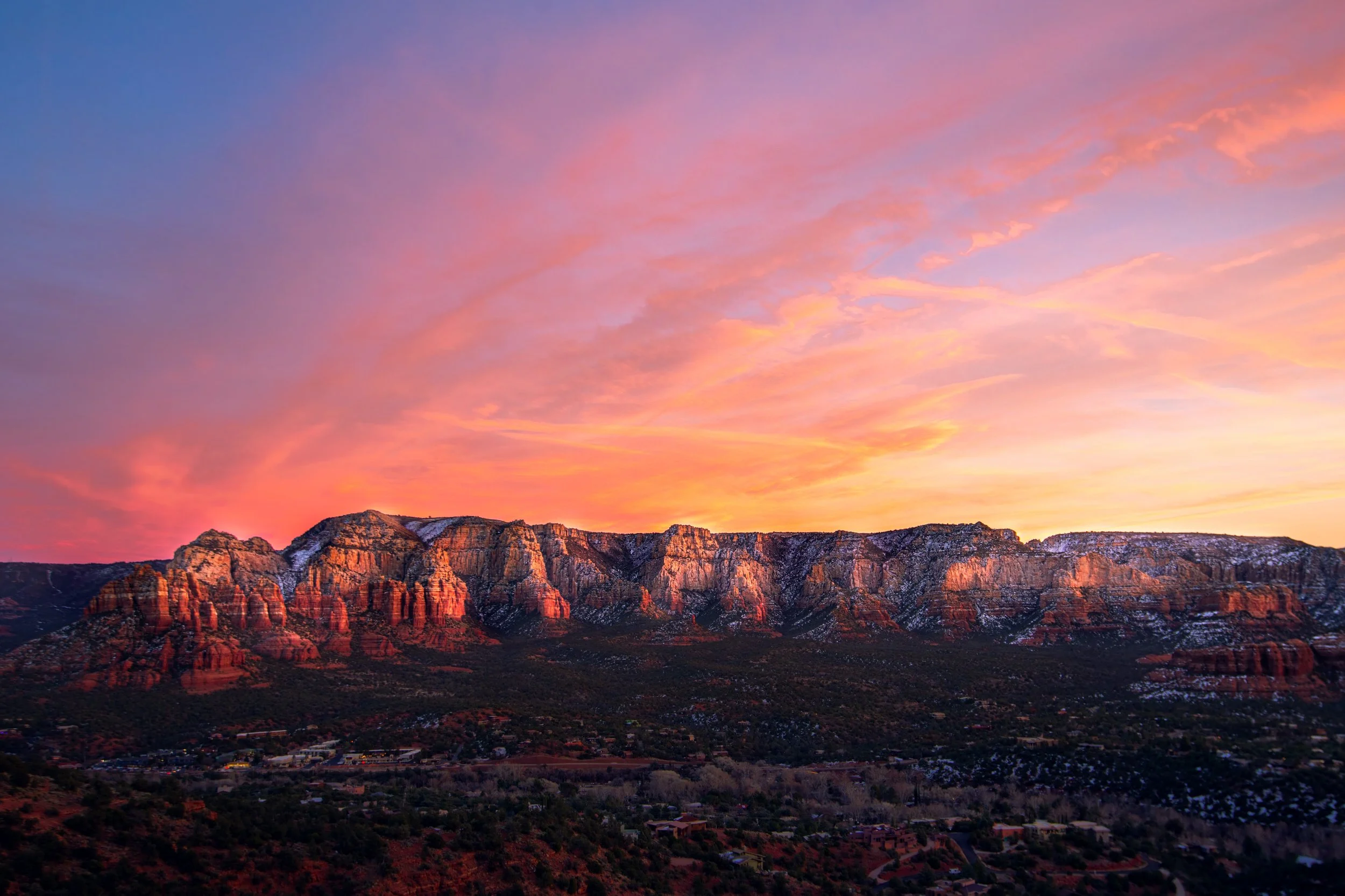 Sunset over a mountain range with pink and orange clouds in the sky and a small town at the base.