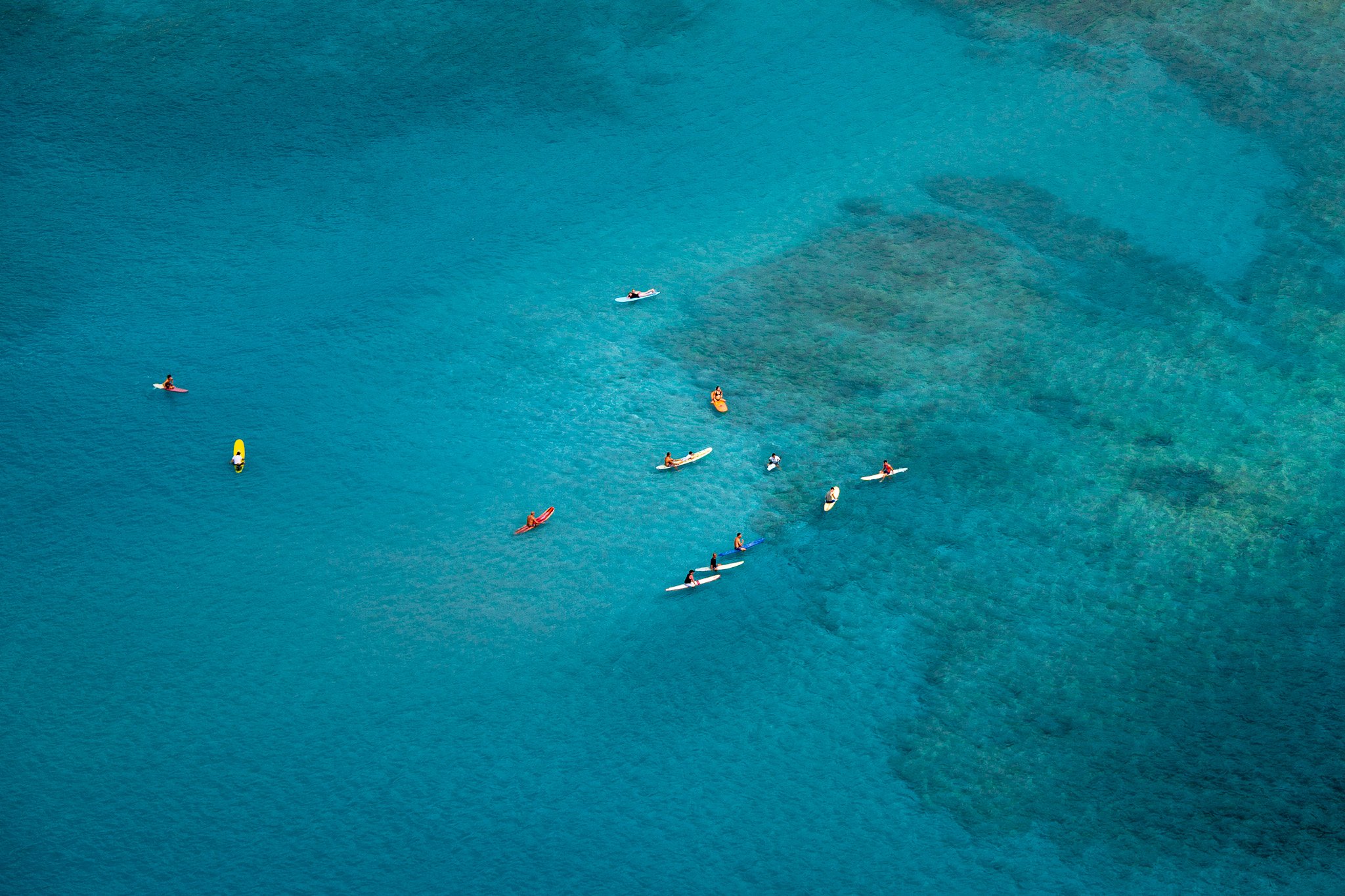 Aerial view of several people paddleboarding and kayaking in clear blue water.