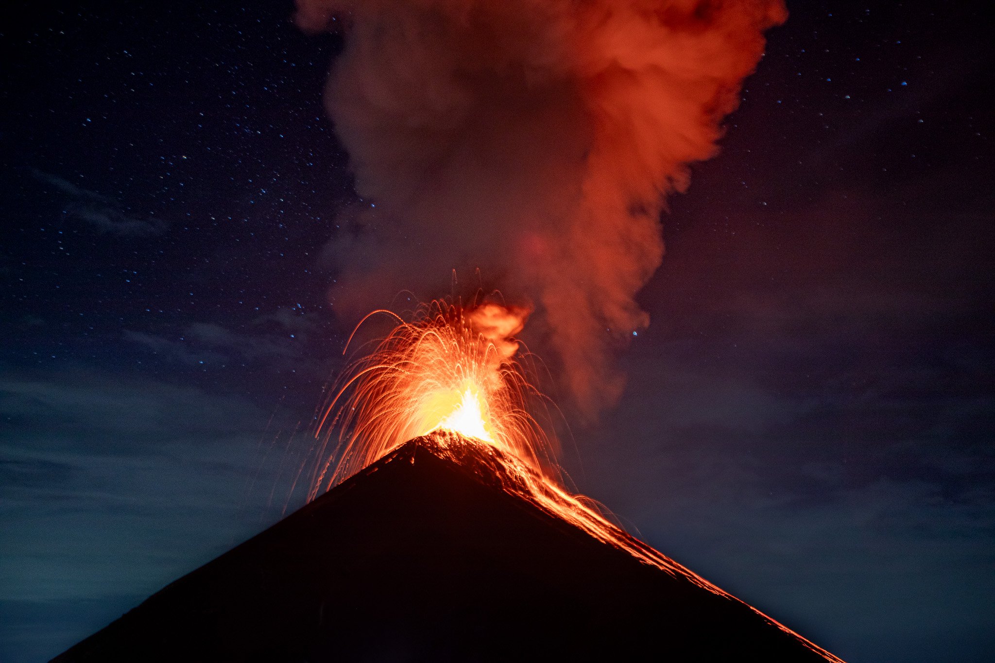 Eruption of a volcano with glowing lava and ash plume against a dark night sky filled with stars.
