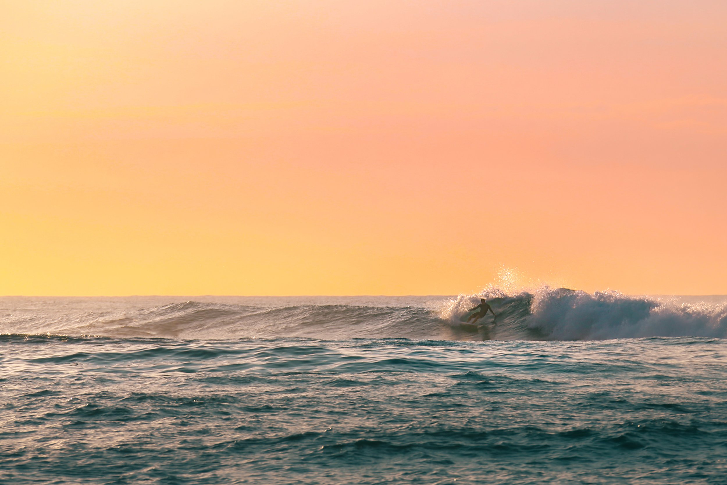 Surfer riding a wave at sunset with a colorful sky in the background.