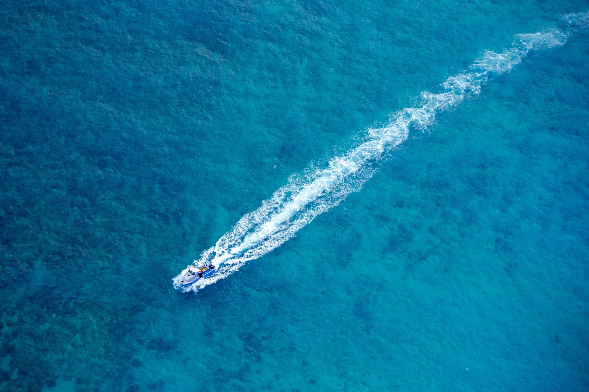 A boat moving across the ocean creating a white wake behind it.