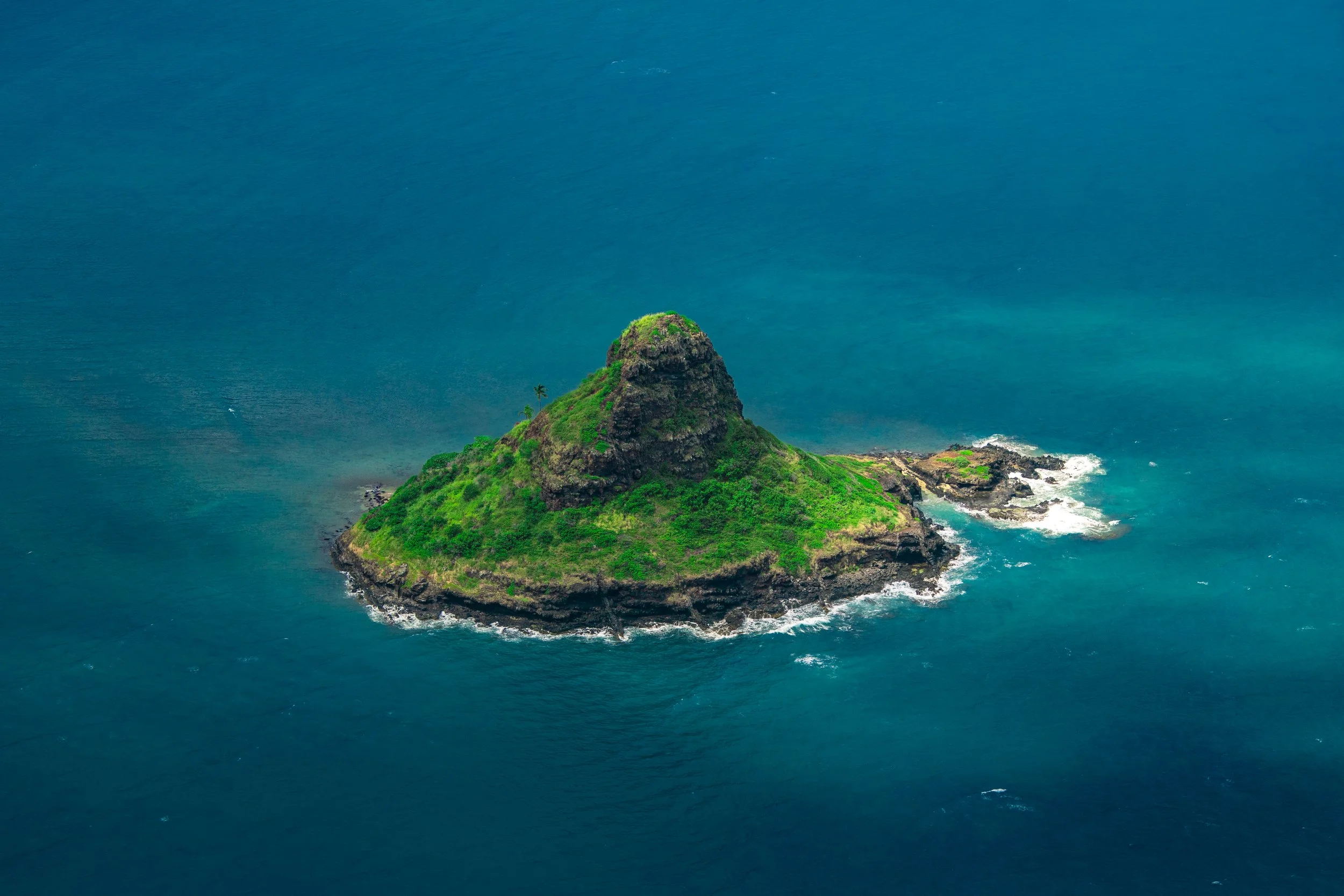 A small island surrounded by blue ocean water, with a rocky peak covered in green vegetation.