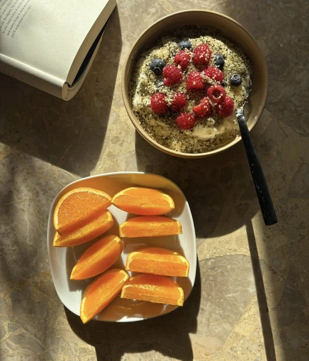A bowl of yogurt topped with berries and a plate of orange slices on a marble surface.