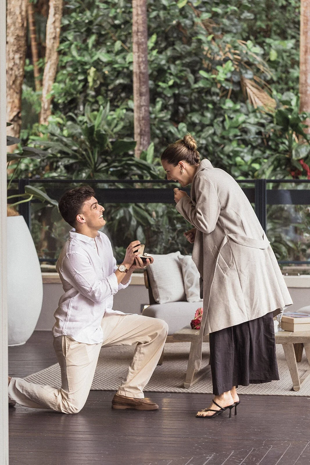 Man proposing on one knee on the deck as the woman reacts, Ben and Chloe's marriage proposal in Byron Bay