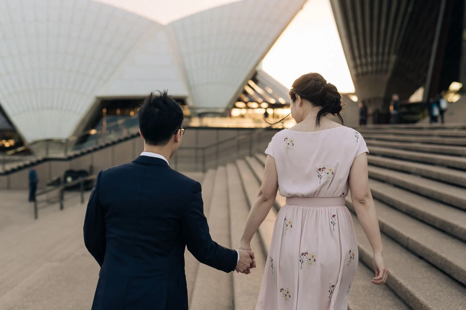 Couple holding hands walking past the Sydney Opera House during their pre-wedding shoot