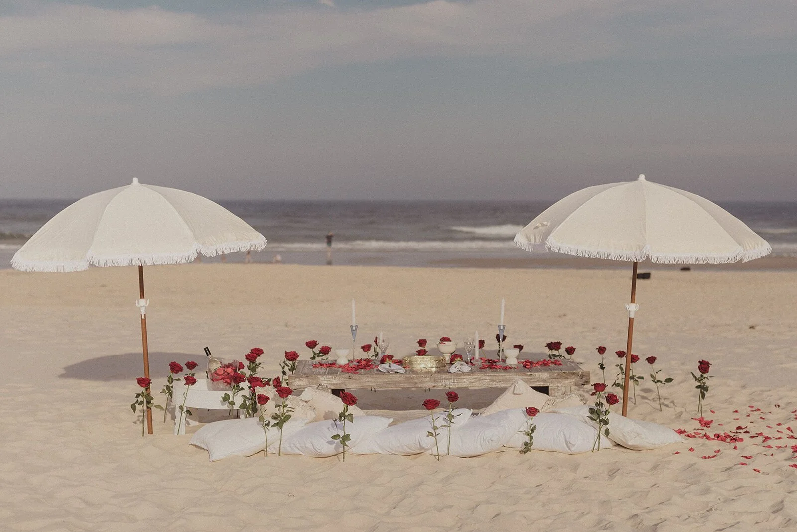 Wide view of the beach proposal set-up with two white fringed umbrellas and red roses, Byron and Luke's marriage proposal at Cabarita Beach, Northern Rivers