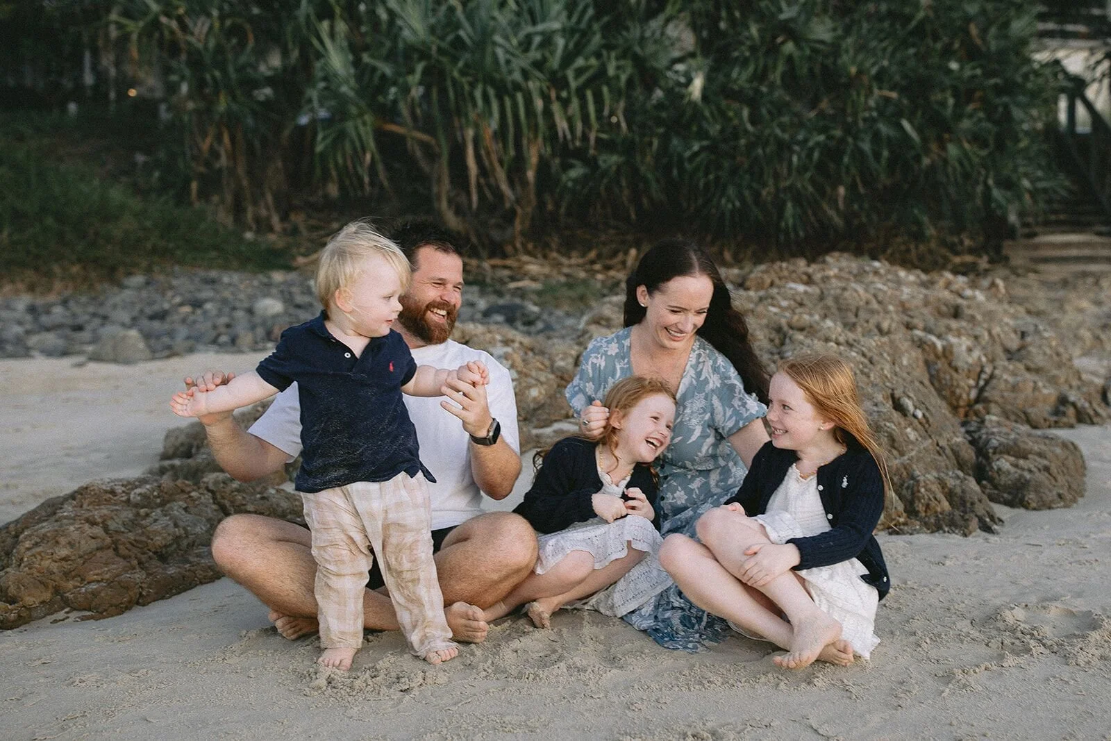 Toddler standing and waving his arms as his family laughs around him on the sand
