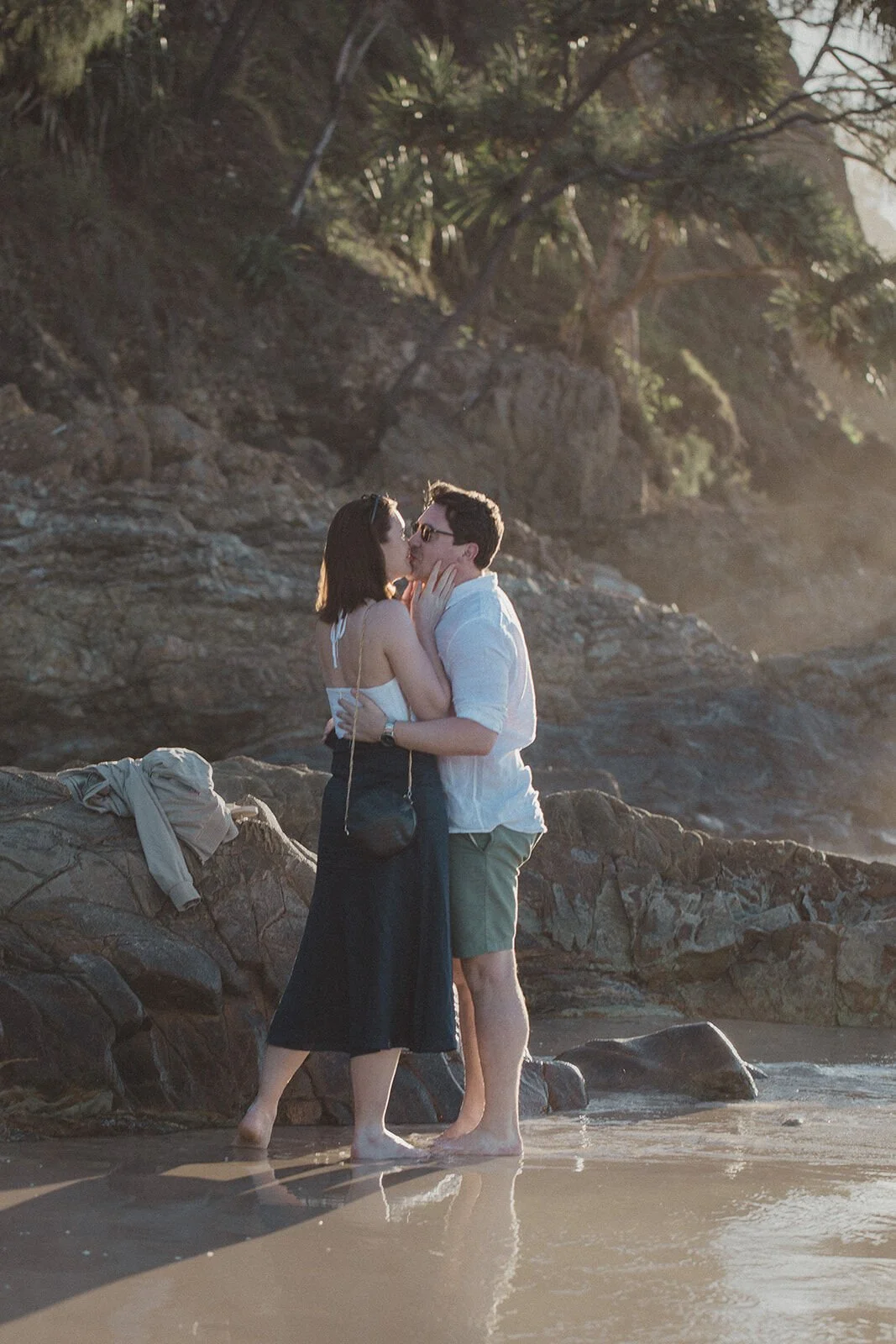 Couple kissing among the rocks right after the proposal, John and Emma's sunset marriage proposal at Wategos Beach, Byron Bay