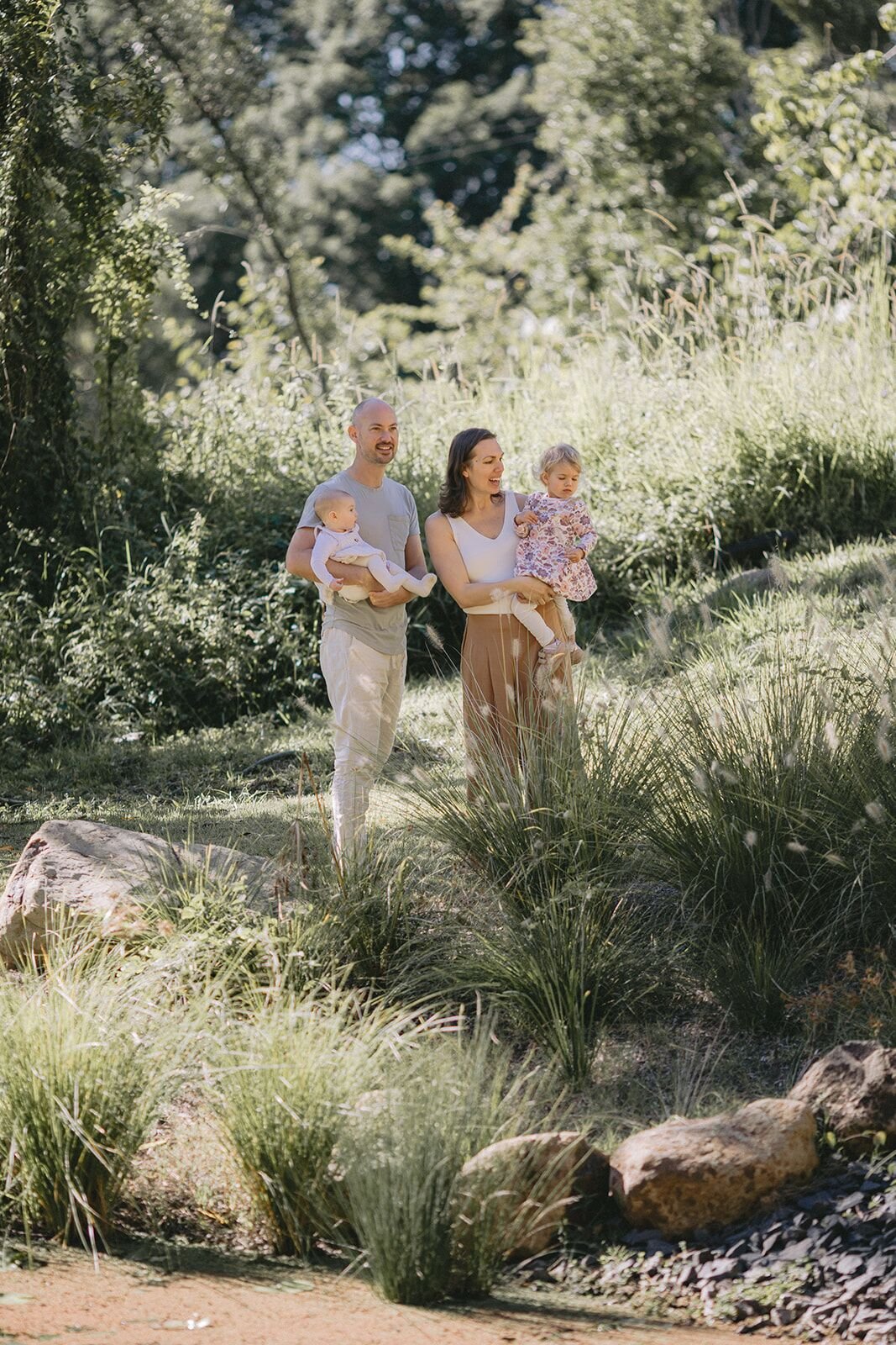 Family of four walking together through long grass and native garden in the hinterland