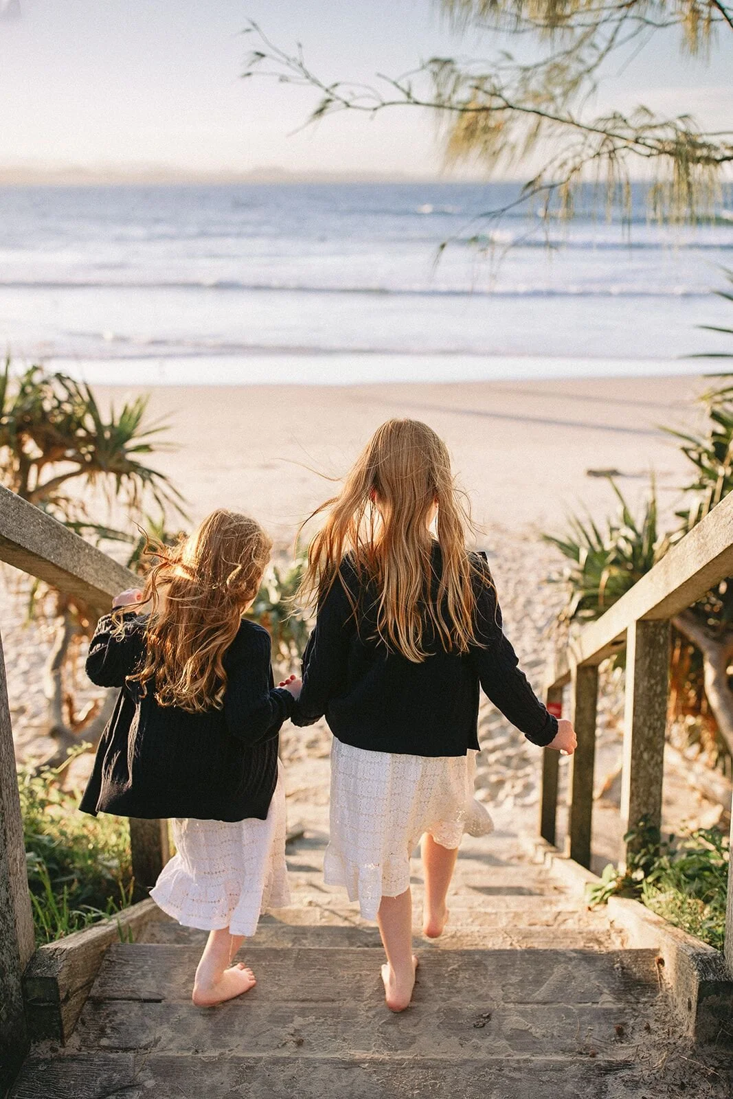 Two sisters holding hands as they walk down the timber steps to Wategos Beach