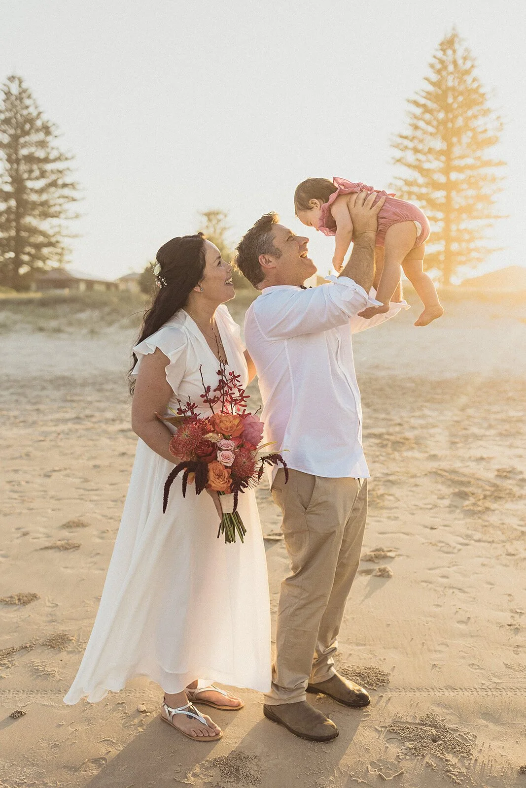 Couple lifting the baby together on the sand at sunset, Maritess and Mark's elopement at Lennox Head