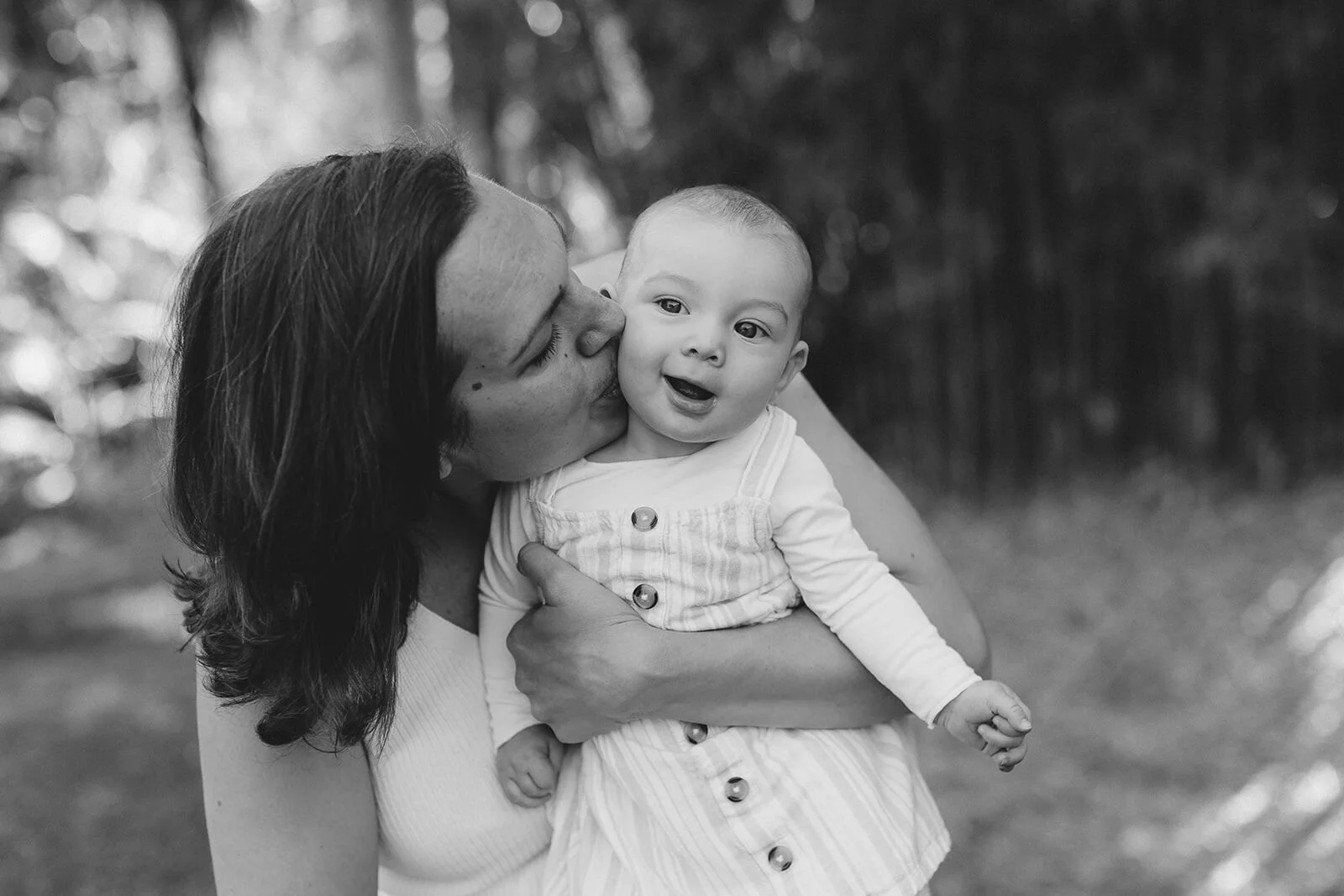 Black and white photo of mum kissing her baby on the cheek in a garden at home