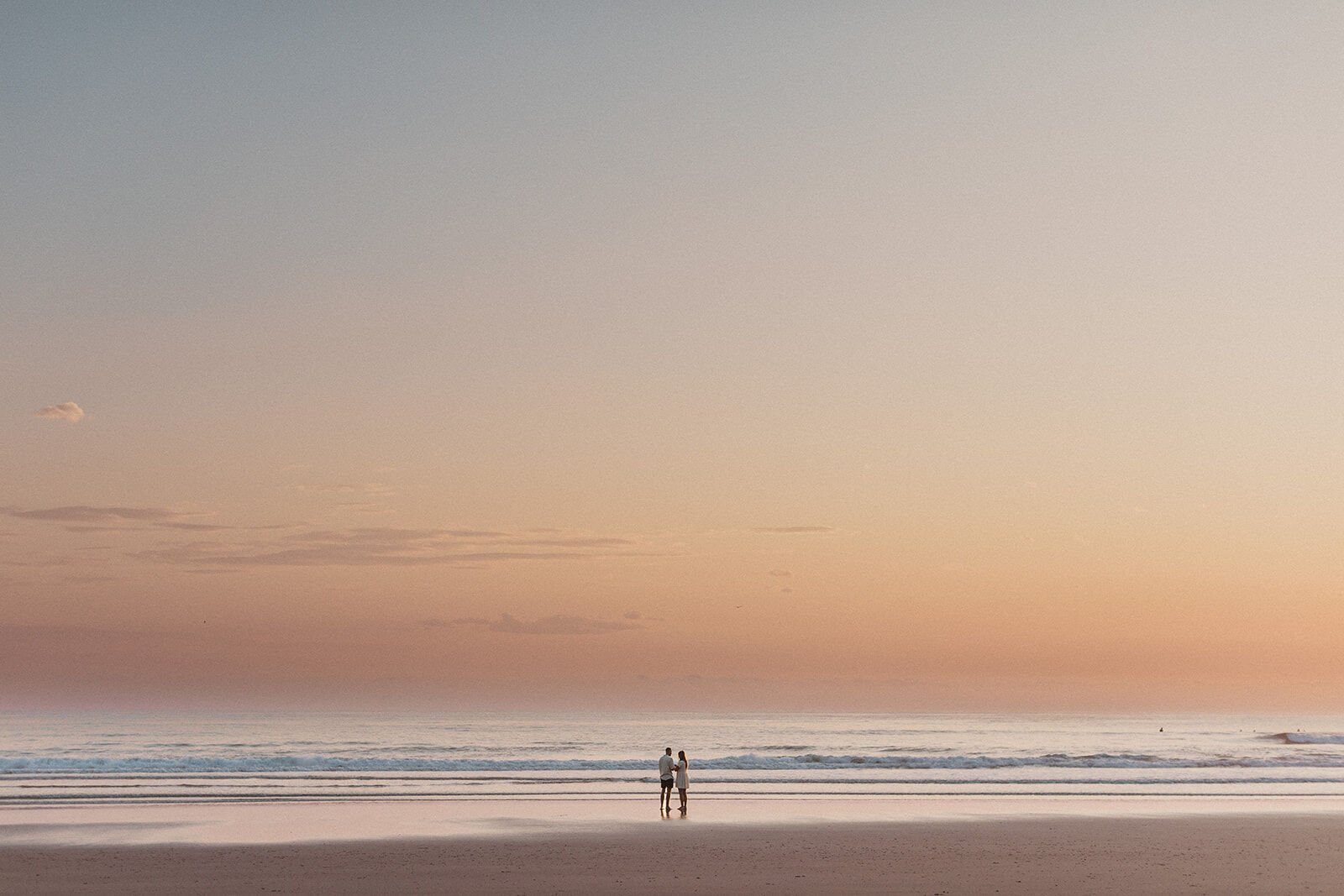 Tiny couple walking along the shoreline beneath a pastel sky, Charlie and Hannah's sunrise marriage proposal at Broken Head Beach, Byron Bay