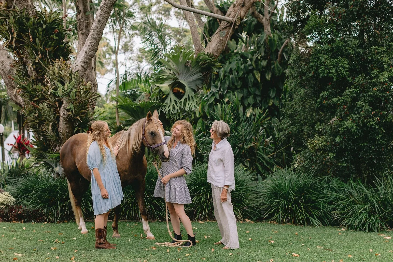 Grandmother and two granddaughters standing with a horse in a lush rainforest garden