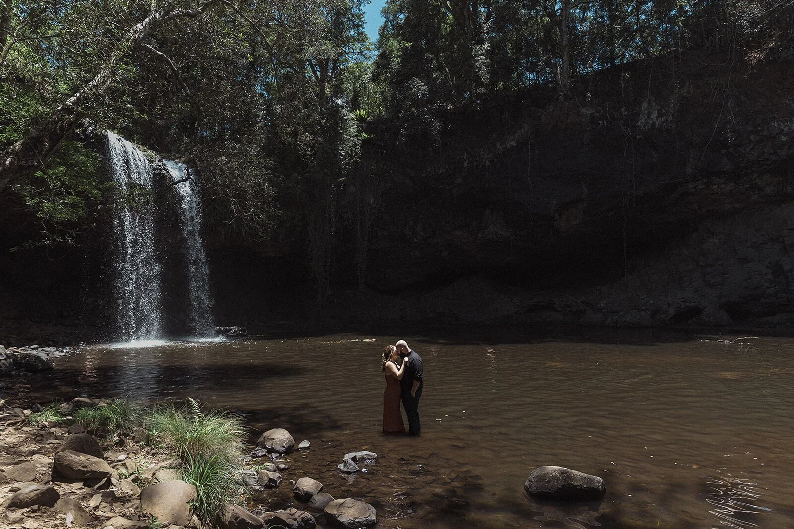 Couple embracing in the distance by the waterfall pool, Sara and Graeme's elopement at Killen Falls, Northern Rivers