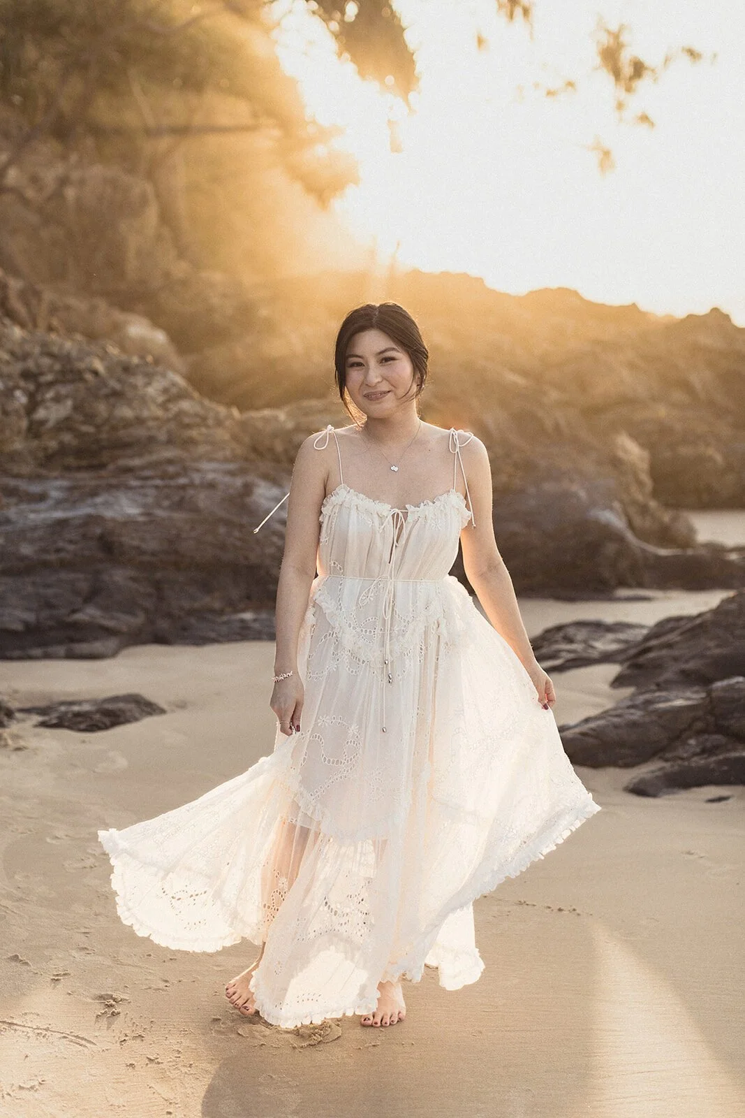 Bride in a white dress smiling on the beach in golden light, Maggie and William's pre-wedding photos in Byron Bay