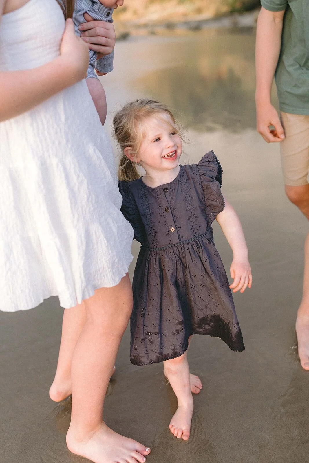 Little girl in a navy dress laughing as she walks barefoot along the shoreline