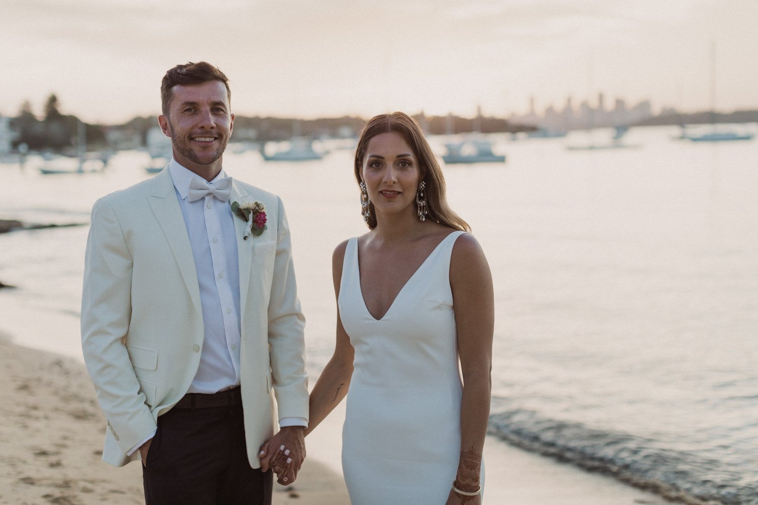 Bride and groom on the sand at Watsons Bay with the Sydney skyline behind