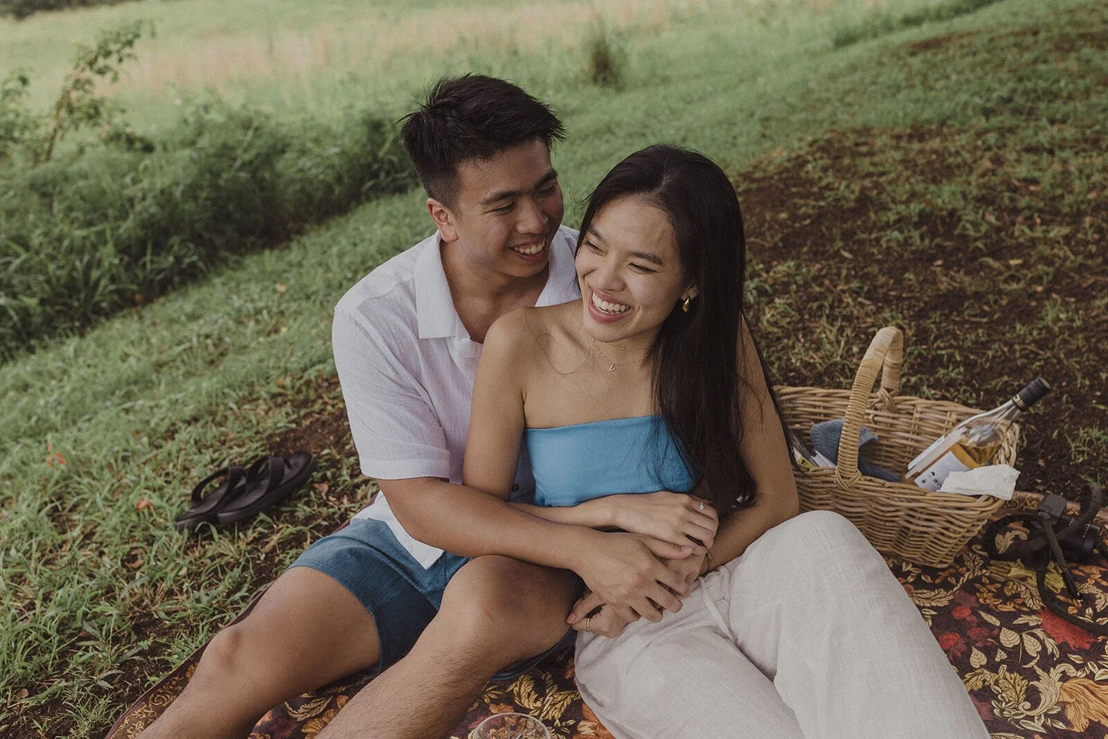 Couple laughing and cuddled up on the rug next to the picnic basket, Darien and Jacqui's picnic marriage proposal at Heartwood Farm, Byron Bay hinterland