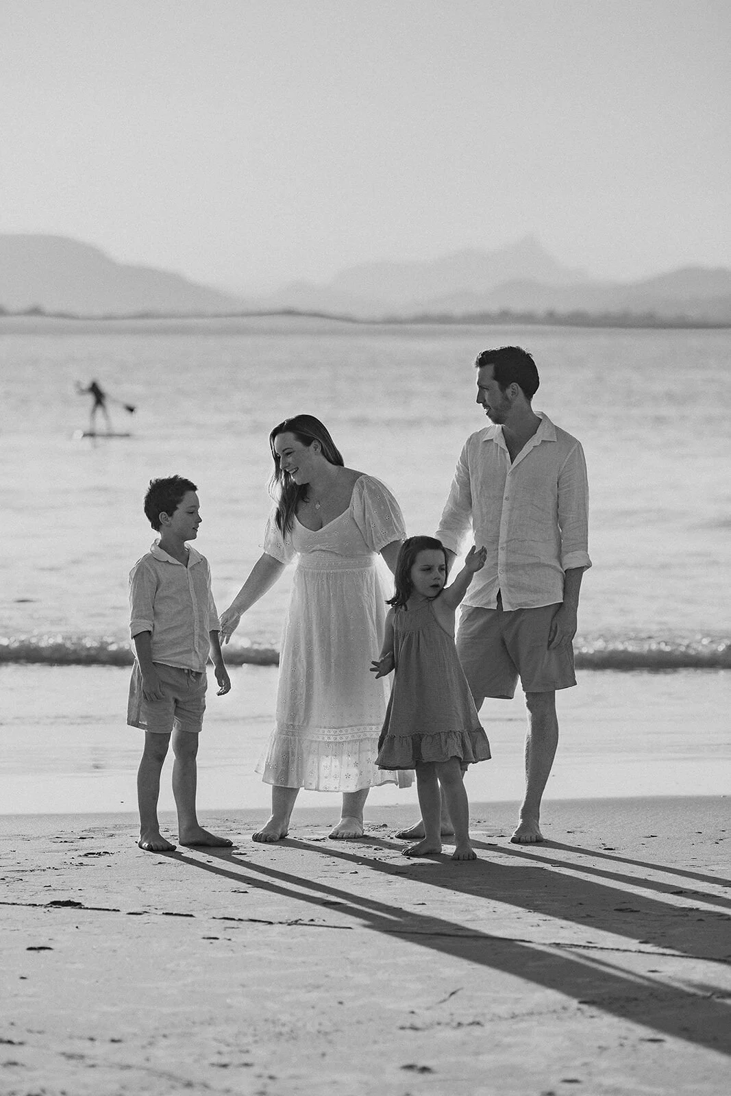 Black and white photo of a family of four standing at the water's edge with Wollumbin in the distance