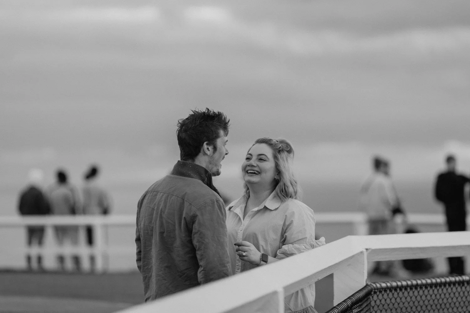Black and white photo of a newly engaged couple laughing at the Byron Bay lighthouse lookout