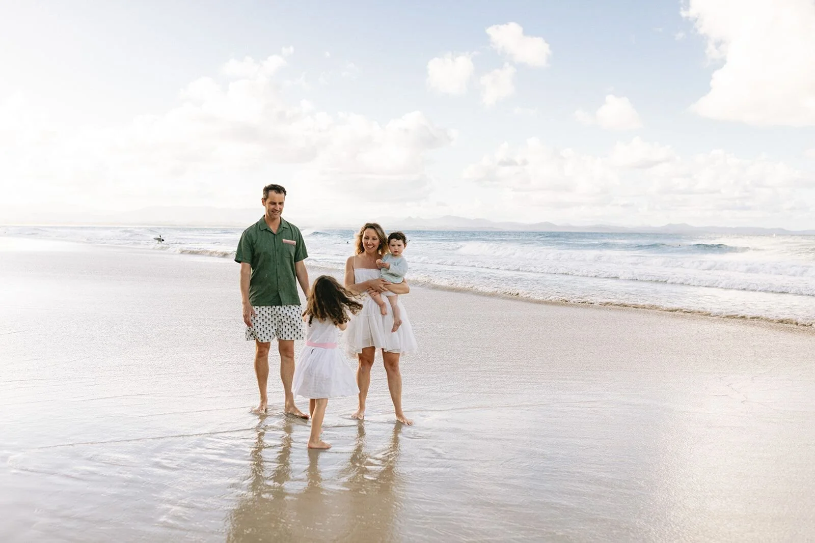 Family walking toward the camera along the wet sand with the Byron Bay coastline behind them