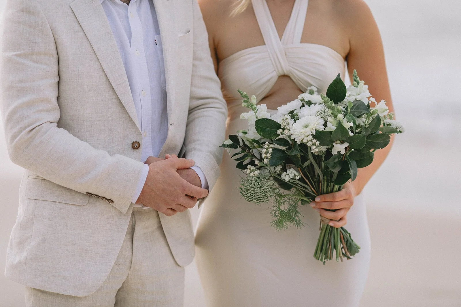 Close detail of the bride's white and green bouquet beside the groom, Abby and James' elopement at Little Wategos Beach, Byron Bay