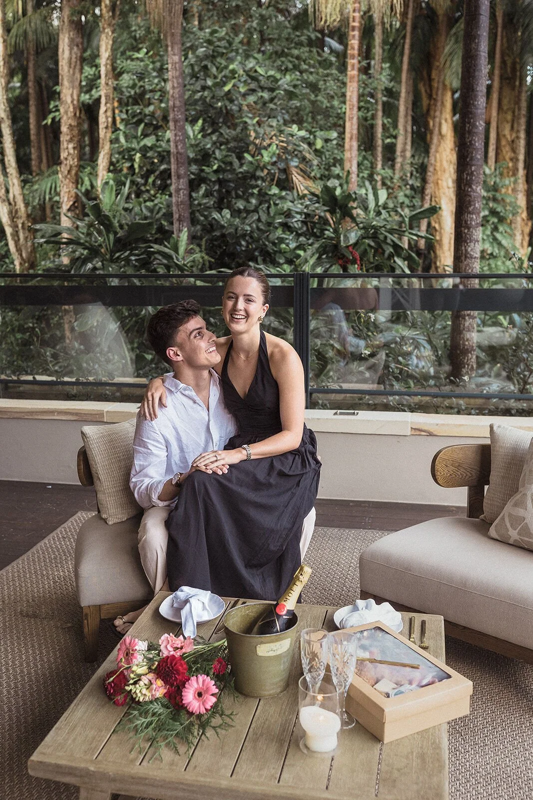 Couple cuddled up on the lounge, her sitting on his lap, Ben and Chloe's marriage proposal in Byron Bay