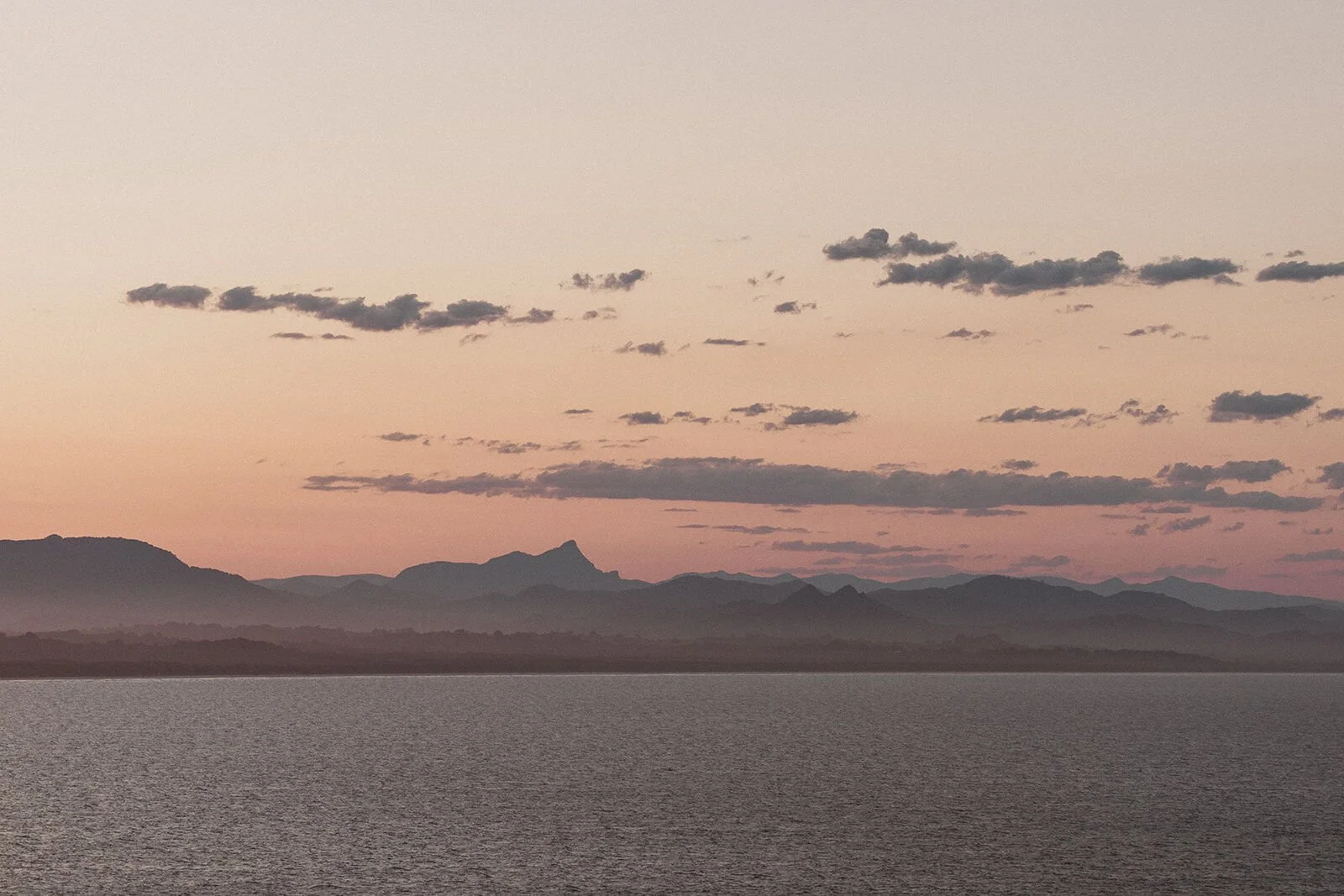 Soft pink sunset sky over the water and distant mountain range, Douglas and Ying's sunset marriage proposal at Cape Byron Lighthouse, Byron Bay