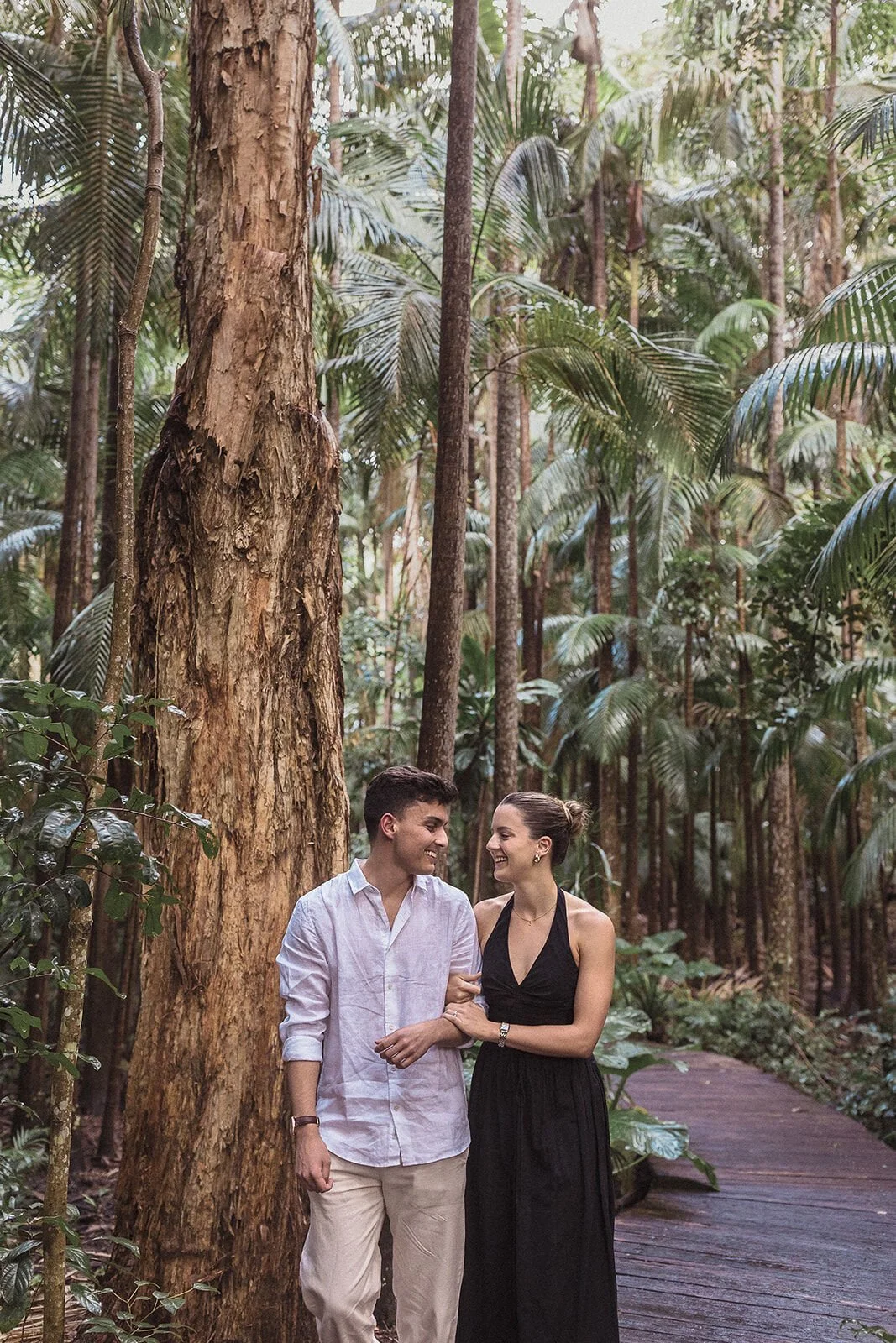 Couple walking arm in arm and laughing beside a big tree, Ben and Chloe's marriage proposal in Byron Bay