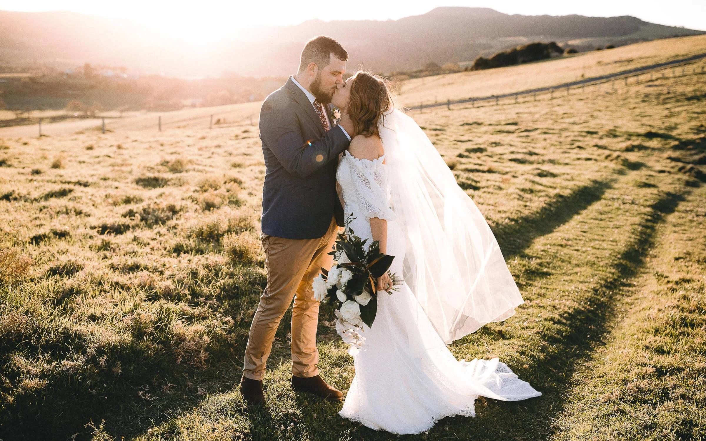 Bride and groom embracing in golden grass at sunset, Gerringong on the NSW South Coast