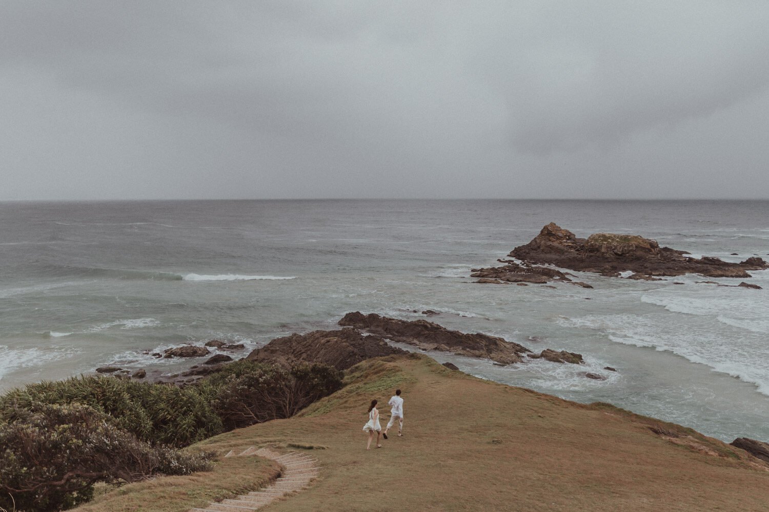 Couple on the grassy headland above the sea, Yoanne and Elisa's rainy elopement at Broken Head, Byron Bay
