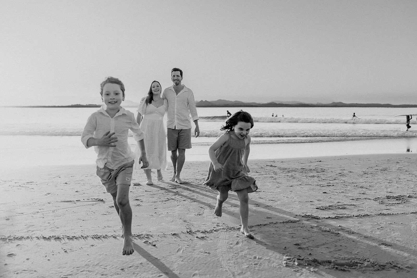 Black and white photo of two kids running toward the camera with their parents behind them
